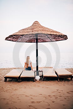 Back View Of Deckchairs, Sun Loungers Under Umbrella On Sand Beach. Woman Relaxing On Lounge Chairs Under Tent By Sea. Girl Enjoyi