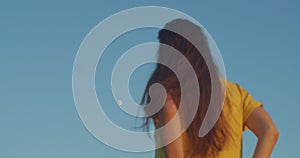 Back view of defocused woman stroking long hair outdoors. Faceless girl watching rising moon in blue sky daylight slow