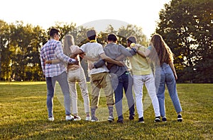 Back view of diverse friends standing in green summer park and hugging each other