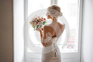 Back view of the elegant blonde bride dressed in a white dress holding a wedding bouquet