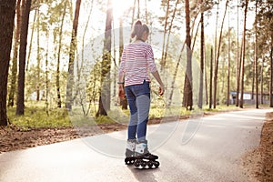 Back view of energetic slender young woman being in middle of road, wearing striped sweatshirt and jeans, having training in fresh