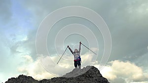 Back view of excited hipster girl standing on high mountain top feeling free raising hands up, happy female traveler