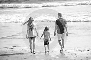 Back view of family on the beach. People having fun on summer vacation. Father, mother and child holding hands against