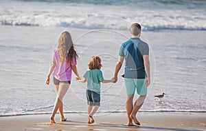 Back view of family on the beach. People having fun on summer vacation. Father, mother and child holding hands against