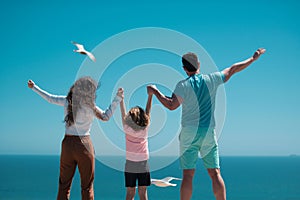 Back view of family on the beach. People on summer vacation. Father, mother and child holding hands against blue sea