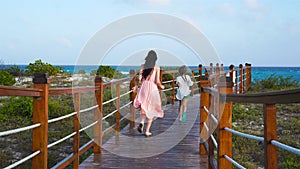 Back view family mother and daughters walking on wooden deck near the beach enjoying tropical summer vacation.