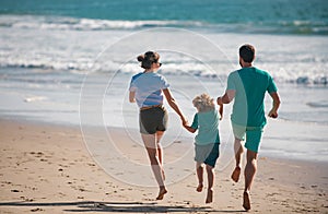 Back view of family run on the beach. People having fun on summer vacation. Father, mother and child holding hands