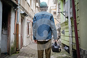 Back view of fashionable young man with vintage cassette player in hand, wandering backstreets of historical city photo