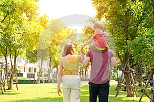 Back view of father, mother with little child in the park on a sunny summer day together. Son sitting on his father shoulders