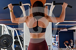 Back view female athlete does back exercises in gym