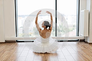 Back view of female ballet dancer sitting in front of panoramic window.