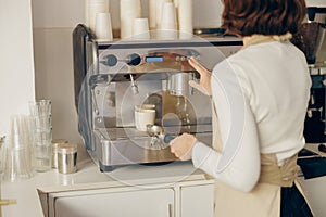 Back view of female barista making coffee in a coffee machine while working in cafe