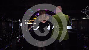 Back view of female Caucasian DJ mixing music as elderly male visitor dancing next to controller. Young woman in black