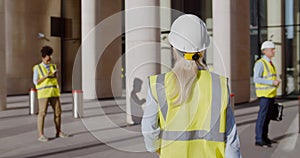 Back view of female engineer in safety hardhat and vest entering office building