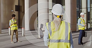 Back view of female engineer in safety hardhat and vest entering office building