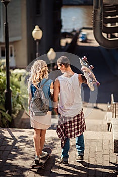 Back view of female and male teenagers with skateboard have active activities outdoor during summer recreation, ride