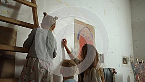 Back view of female painter and children painting on wall with black chalk.