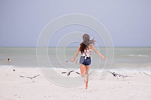 Back view of female running on sandy beach surrounded by seagulls in background of sea