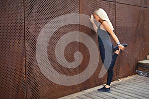 Back view of fit woman stretching after workout against metal wall in the city