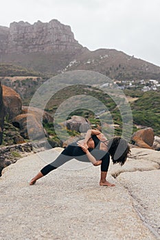 Back view of flexible slim female standing on mat and performing bound revolved crescent lunge pose against beautiful landscape