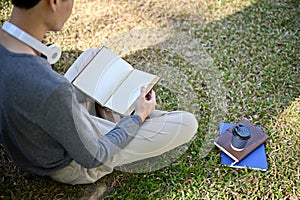 Back view, Focused young Asian male college student reading a book, relaxing in the campus park