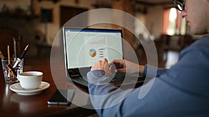 Back view of freleancer businessman in glasses diligently working on laptop in cafe. Man typing on keyboard of computer