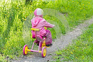 Back view full length portrait of little girl riding kids pink and yellow tricycle on park track