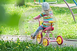 Back view full length portrait of preschooler girl riding kids pink and yellow tricycle on playground track photo