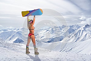 Back view of girl in bikini holding snowboard above head