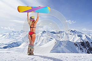 Back view of girl in bikini holding snowboard above head