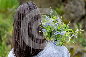 Back view of a girl with a bouquet of wild forest flowers