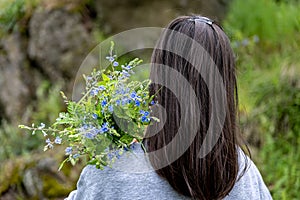 Back view of a girl with a bouquet of wild forest flowers