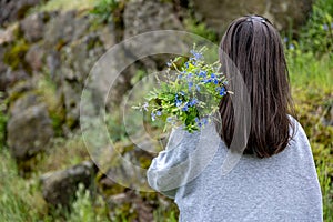 Back view of a girl with a bouquet of wild forest flowers
