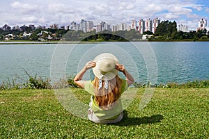 Back view of girl with hat sitting on grass in Barigui Park, Curitiba, Brazil photo