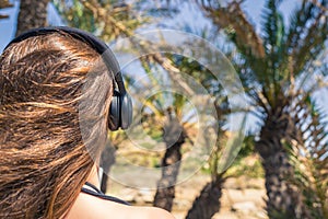 Back view on the girl in the headphones listening music  walks in the palm forest. Seychelles islands.
