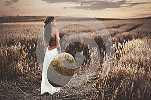 Back view of girl holding shield among grass in field.