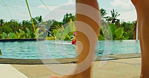 Back view of girl legs go into the swimming pool. Woman in a bathing suit enters the water. Cocktail glass poolside