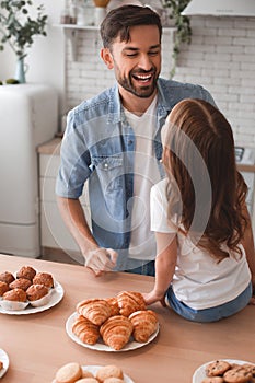 Back view of girl sitting on the kitchen table and laughing with father together