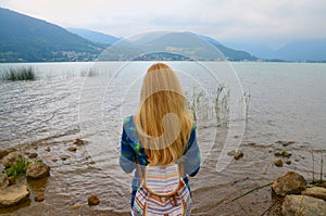 Back view of girl standing near water and looking at horizon with mountains