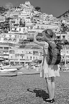 Back view of a girl take photo on the beach in Positano. View of houses and hotels in the background. Travel and vacation. Black