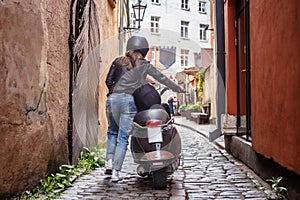 Back view of a girl walking with a scooter along the old narrow streets of Latvia.