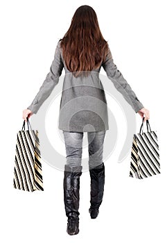 Back view of going woman in jacket with shopping bags