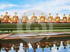 Back view of golden monk statues sitting with water reflection a