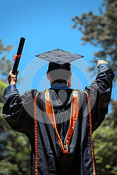 Back view of a graduate with diploma and cap outdoors. Graduation time in educational institutions. photo