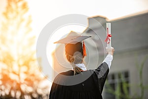 Back of view Graduate put hands up and celebrating with certificate in her hand and so proud