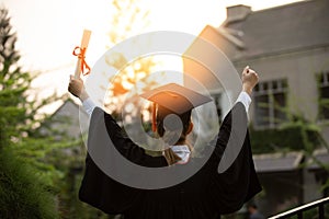 Back of view Graduate put hands up and celebrating with certificate in her hand and so proud and happiness in Commencement day