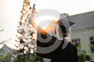 Happy graduated young woman in cap and gown talking with parent in mobile phone and looking certificated in hand so proud