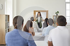 Back view of group of adult students sitting in classroom and listening to teacher