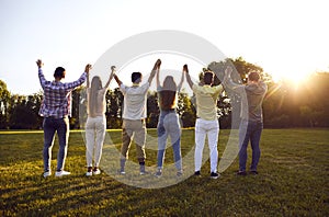 Back view of a group of friends standing in a row holding hands with their hands up outdoors.