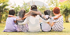 Back view, Group of kindergarten multi ethnic kids friends arm around sitting together at park outdoor - Concept showing